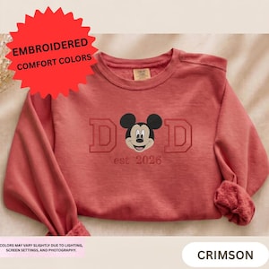A red sweater with a Mickey Mouse design and the text "DAD est 2026" printed on it.