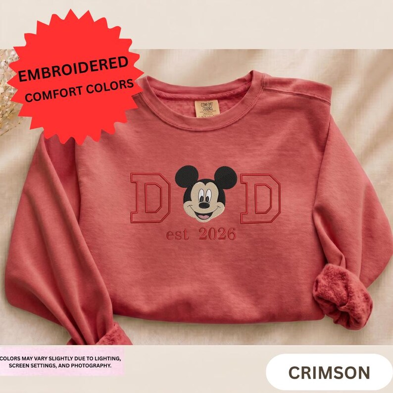 A red sweater with a Mickey Mouse design and the text "DAD est 2026" printed on it.