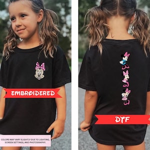 a young girl wearing a black t-shirt with Minnie Mouse designs on the back. The t-shirt is embroidered with Minnie Mouse characters, and the girl is smiling.
