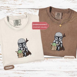 two t-shirts with embroidered characters from the Star Wars franchise, specifically the Mandalorian and Baby Yoda.