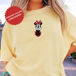 A person wearing a yellow t-shirt with a Minnie Mouse embroidered on it.