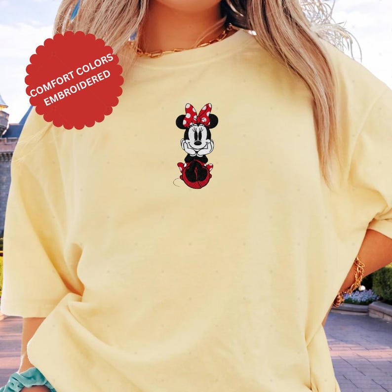 A person wearing a yellow t-shirt with a Minnie Mouse embroidered on it.