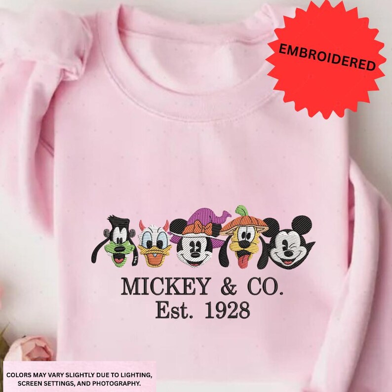 A pink t-shirt with a graphic design featuring the characters Mickey Mouse, Donald Duck, Goofy, and Pluto, along with the text "MICKEY & CO. Est. 1928".