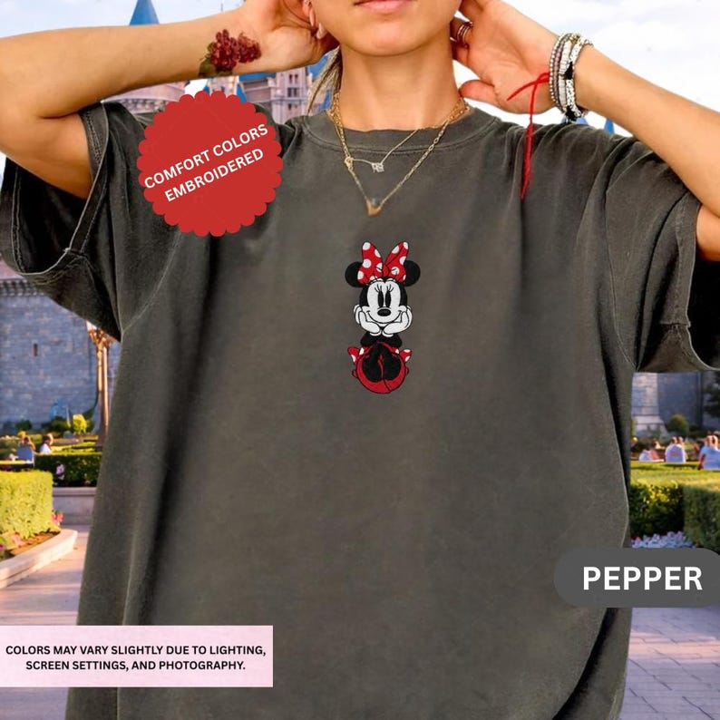 A person wearing a gray t-shirt with a Minnie Mouse embroidered on it, standing in front of a cityscape.