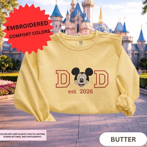 A yellow t-shirt with a Mickey Mouse design and text, along with a castle in the background, is displayed.