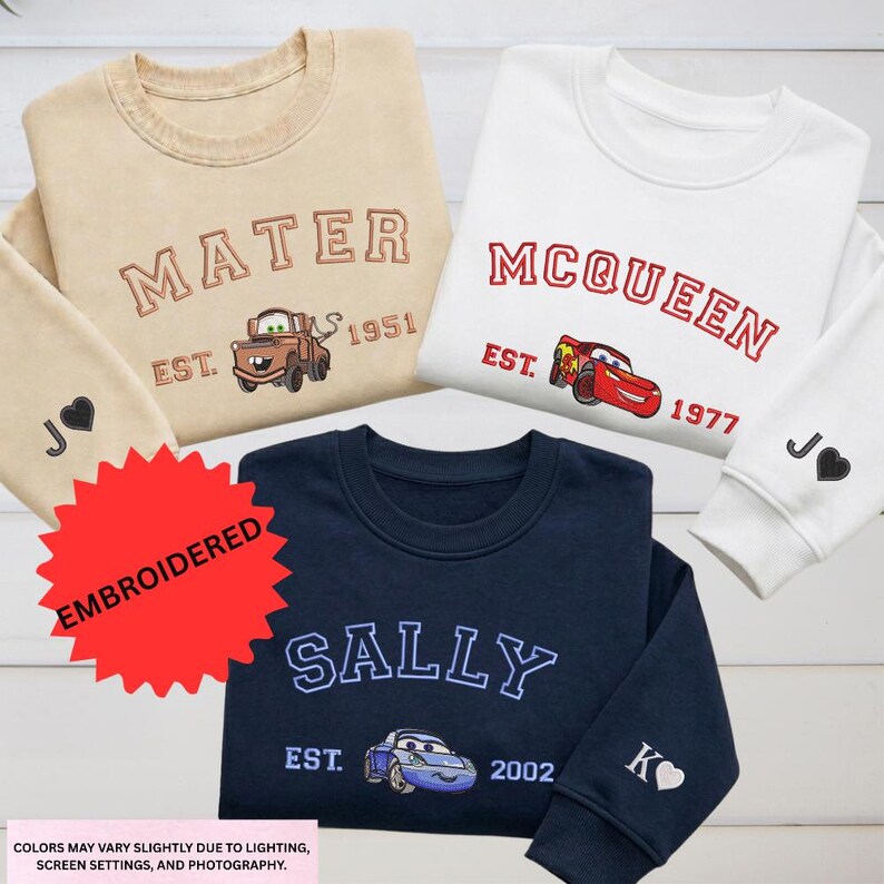three children's sweatshirts with the character Sally from the Cars movie, each with a different color and design. The sweatshirts are embroidered with the character's name and the year 1977.