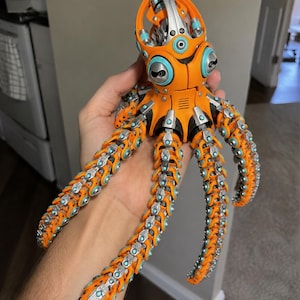 Pode incluir: Uma figura de polvo mecânico com um esquema de cores laranja brilhante e prateado com detalhes circulares em azul claro. A criatura articulada tem uma cabeça arredondada e oito tentáculos segmentados e flexíveis dispostos radialmente.