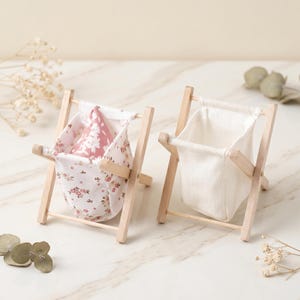 May include: Two miniature wooden beach chair-style storage baskets. One basket features a floral print fabric in pink and white, while the other has a plain white fabric. The wooden frames are light-colored.