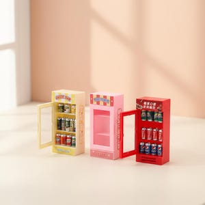 May include: Three miniature vending machines in yellow, pink, and red. The yellow machine has "JUICE BAR" text and is filled with small cans. The pink machine is empty. The red machine has soda cans.