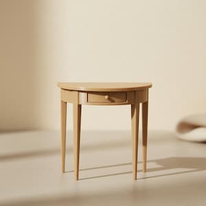 May include: A small, half-moon shaped table in a light tan color. The table has a single drawer with a small, round knob. It has four slender, tapered legs. The table is a miniature furniture piece.