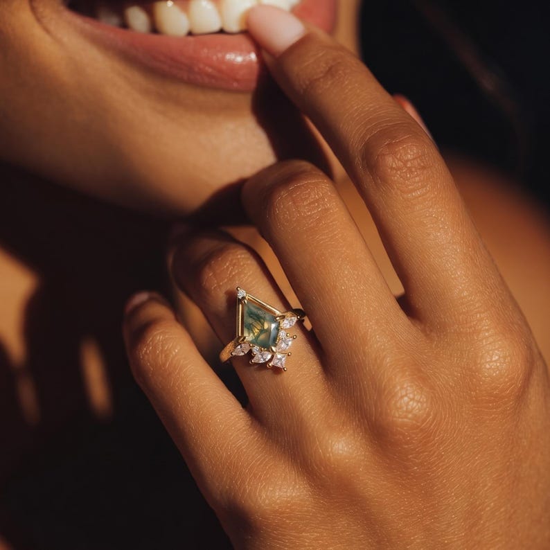 Puede incluir: Un anillo de oro con una gema verde en forma de cometa y peque&ntilde;as piedras claras. El dise&ntilde;o del anillo es intrincado y detallado. El anillo se lleva en un dedo. La gema verde tiene un patr&oacute;n &uacute;nico.