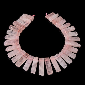 May include: A strand of pink rose quartz beads, each bead is a rectangular prism with a smooth, polished finish. The beads are strung on a thin pink thread.