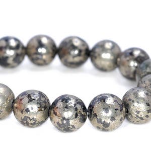 Pode incluir: Um bracelete feito de contas redondas prateadas com um padrão salpicado de preto e branco.