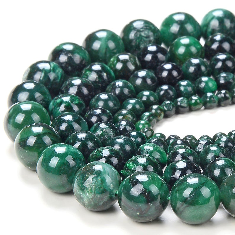 May include: A strand of green malachite beads, each bead is round and polished, with a smooth, glossy finish. The beads are arranged in a circular pattern, with the largest beads in the centre and the smallest beads on the outside.