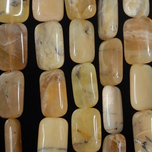May include: Close-up of a collection of rectangular, polished gemstones. The stones are a creamy yellow color with subtle brown and gray veining, giving them a natural, earthy appearance. The gemstones are strung together, suggesting they are intended for jewelry making.