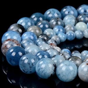 May include: A strand of light blue aquamarine beads with a mottled, cloudy appearance. The beads are round and smooth, and they are arranged in a circle.