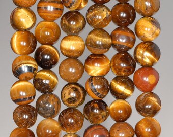 May include: A collection of polished tiger's eye gemstone beads. The beads are spherical, with a warm, golden-brown color and chatoyant bands that create a shimmering effect. The beads vary in color and pattern, with some displaying darker brown and black streaks.