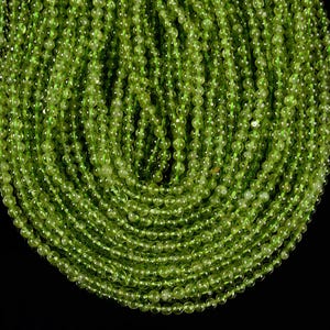 Op de afbeelding: Een streng groene peridot kralen, elke kraal is rond en glad. De kralen zijn in een cirkelvormige patroon gerangschikt, waardoor een visueel aantrekkelijk display ontstaat.