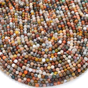 May include: A strand of round, multi-colored gemstone beads. The beads are a mix of brown, red, green, yellow, and white. The beads are all approximately the same size.