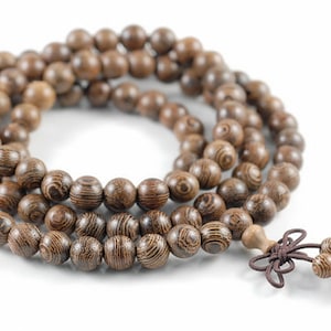 May include: A strand of wooden prayer beads with a brown finish. The beads are round and have a striped wood grain pattern. A tassel of smaller beads and a knotted cord are attached.