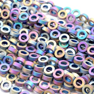 May include: A strand of iridescent, round, donut-shaped beads. The beads are made of hematite and have a metallic finish. The beads are a mix of blue, purple, and gold colors.