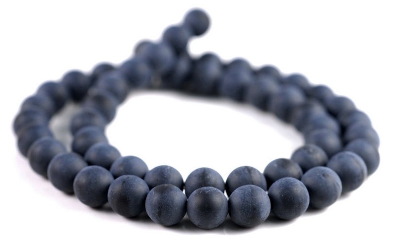 May include: A strand of dark blue matte round beads. The beads are strung together on a cord and are arranged in a circle.