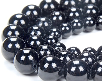 May include: A strand of black gemstone beads. The beads are round and smooth, with a high polish. They are arranged in a circle, with the largest beads in the center and the smaller beads on the outside.