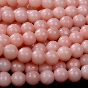 May include: A strand of pale pink round beads. The beads are smooth and have a slight sheen.