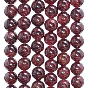 May include: Close-up of a strand of polished, round, dark red garnet beads. The beads are evenly sized and have a glossy finish, reflecting light. The beads are strung together, ready for jewelry making.
