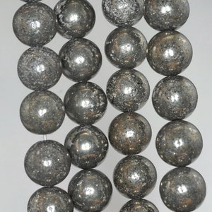 May include: Strands of metallic gray pyrite beads. Each bead is spherical, with a textured, reflective surface. The beads are strung together, creating a necklace or bracelet component. The beads are approximately 10mm in diameter.