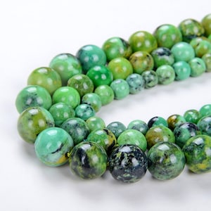 May include: A strand of green gemstone beads with dark green and yellow marbling. The beads are round and smooth, and they are strung on a clear thread.