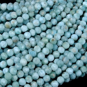Puede incluir: Primer plano de un conjunto de cuentas redondas y facetadas de color azul verdoso pálido. Las cuentas son ligeramente translúcidas y están ensartadas, creando una superficie texturizada. Cada cuenta mide aproximadamente 0,6 cm de diámetro.