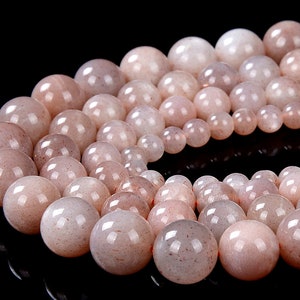 May include: A strand of light pink sunstone beads. The beads are round and have a smooth, polished finish. The beads are strung on a clear elastic cord.