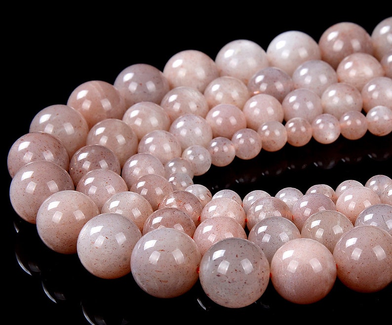 May include: A strand of light pink sunstone beads. The beads are round and have a smooth, polished finish. The beads are strung on a clear elastic cord.
