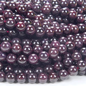 May include: A close-up of a strand of round, dark purple gemstone beads. The beads are smooth and shiny, with a slight sparkle.