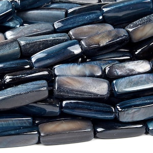 May include: A close-up of a pile of dark blue and gray gemstone beads. The beads are rectangular and have a smooth, polished finish.