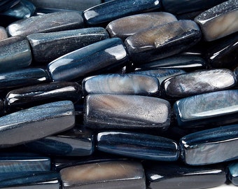 May include: A close-up of a pile of dark blue and gray gemstone beads. The beads are rectangular and have a smooth, polished finish.