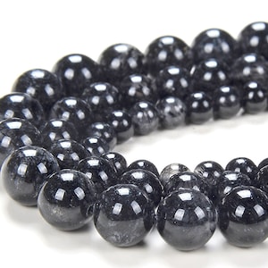 May include: A strand of black gemstone beads with a silver-grey shimmer. The beads are round and smooth, and they are strung on a clear thread.