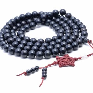 May include: A black wooden mala bead necklace with a red tassel and a knot charm. The beads are round and smooth.