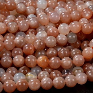 May include: A close-up of a strand of orange sunstone beads. The beads are round and have a smooth, polished finish. The beads are all approximately the same size and are arranged in a random pattern.