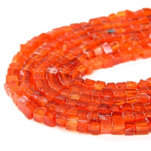 May include: A strand of orange carnelian beads, each bead is a square shape with a slightly faceted surface.