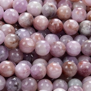 May include: A close-up of a pile of round, smooth, lavender-colored gemstone beads. The beads have a subtle shimmer and a slightly translucent appearance.