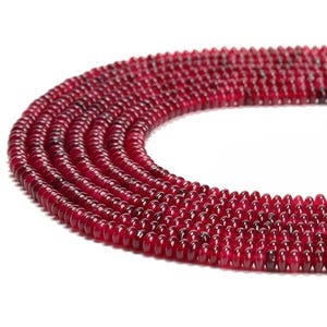 May include: A strand of deep red gemstone beads. The beads are round and smooth, and they are strung together on a clear thread. The beads are all the same size and shape, and they are arranged in a symmetrical pattern.