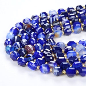 Könnte beinhalten: Eine Strähne aus blauen Achat-Edelsteinkugeln mit goldenen Akzenten. Die Perlen sind facettiert und haben verschiedene Blautöne.