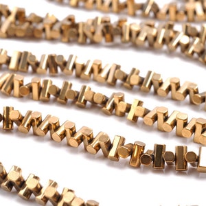 Puede incluir: Primer plano de una cadena de oro hecha de pequeñas piezas de metal interconectadas. La cadena está hecha de una serie de pequeñas piezas rectangulares que están conectadas entre sí en un patrón de zig-zag.