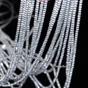 May include: A strand of silver-toned faceted beads. The beads are small and round, and they are strung together on a clear thread. The beads are arranged in a loose, flowing pattern.