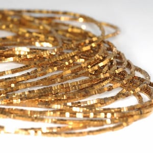 Peut inclure: Un brin de perles carrées de couleur dorée. Les perles sont petites et ont un éclat métallique.