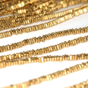 May include: A strand of gold-colored metal beads, each bead is a small, rectangular prism with a slightly pointed end. The beads are strung together to form a long chain.