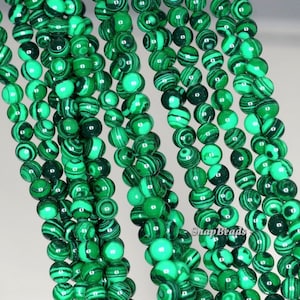 Può includere: Una collana di perle di malachite verde. Le perle sono rotonde e hanno una finitura liscia e lucida. La malachite è una pietra naturale con un caratteristico motivo verde e nero.