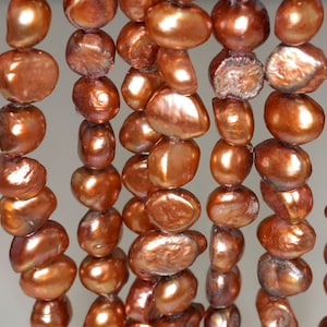 May include: A strand of brown freshwater pearls with a slightly iridescent sheen. The pearls are irregular in shape and have a natural, organic look.